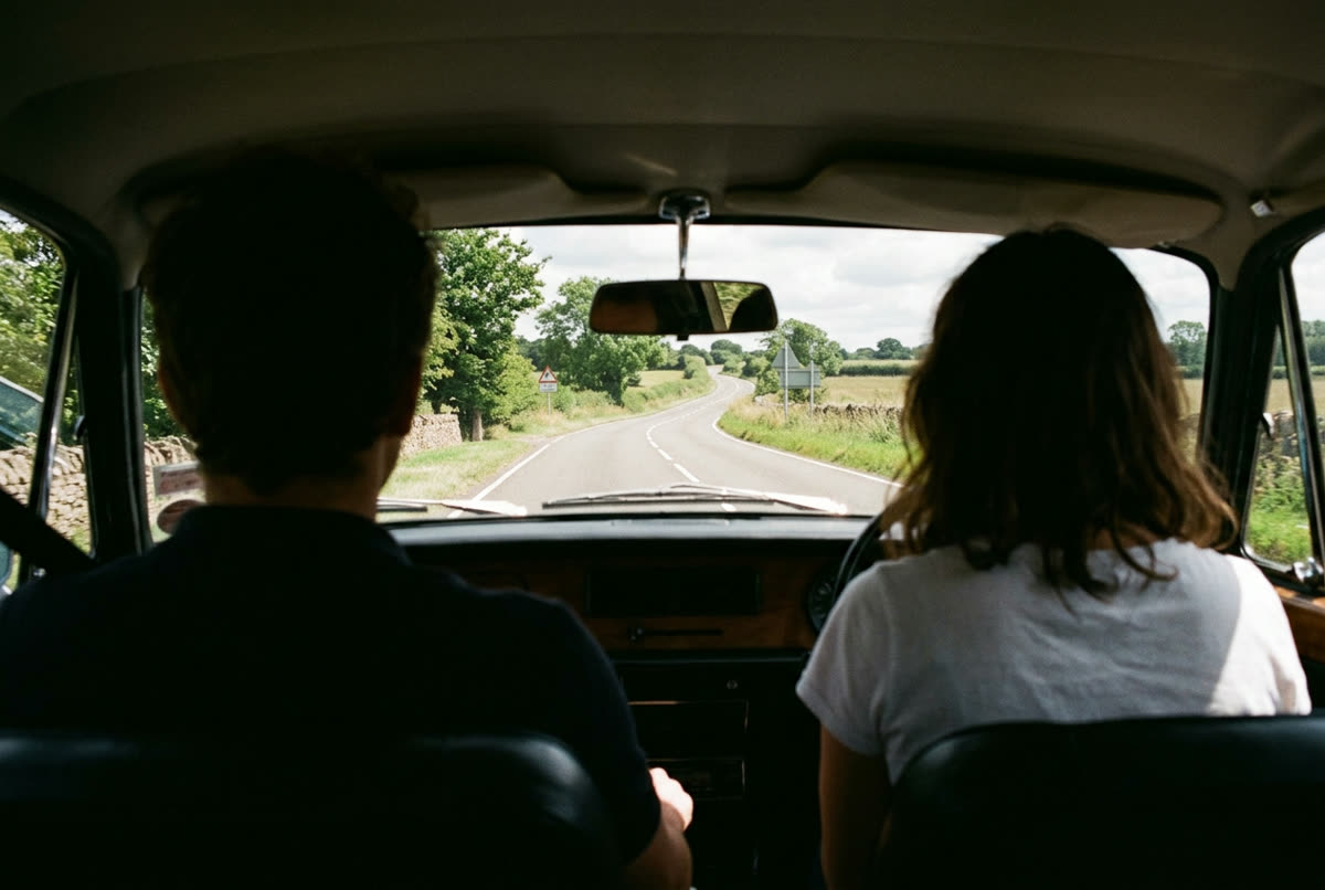 A country road seen through a windscreen from the back seat of a car.