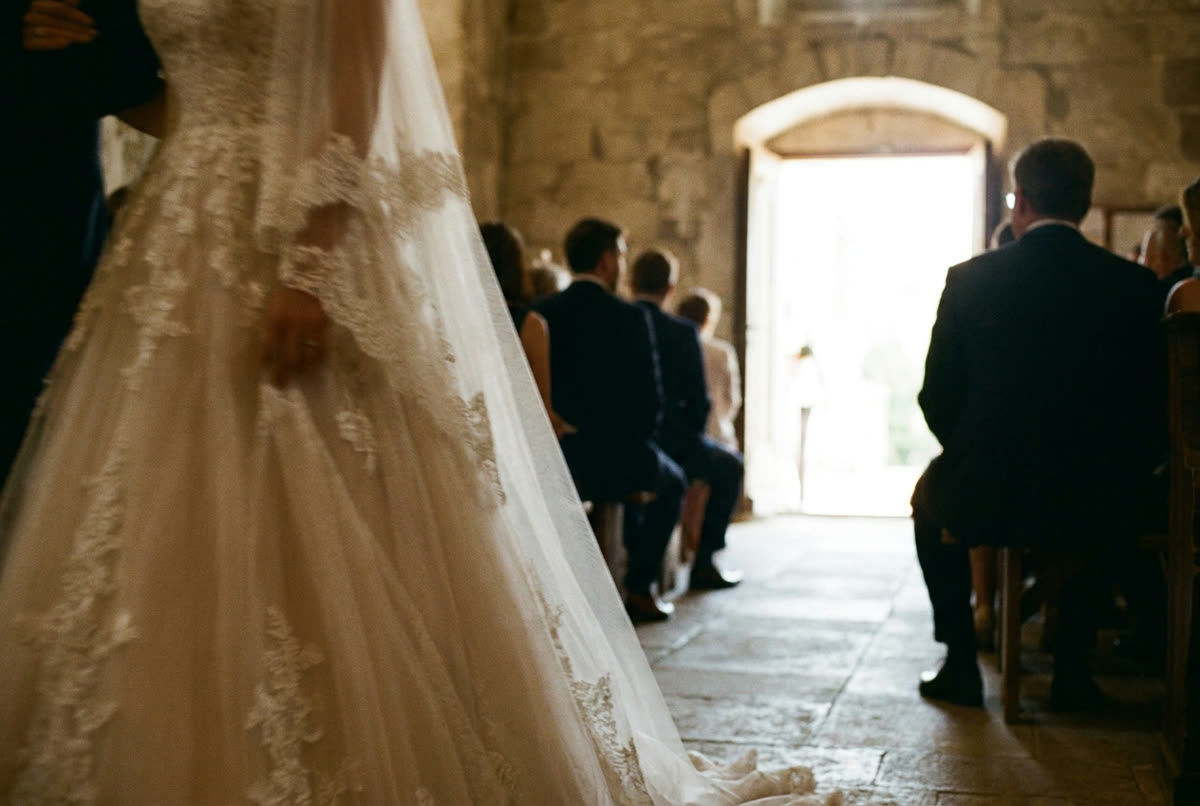 A bride walking past close to camera, guests behind her turned toward the front.