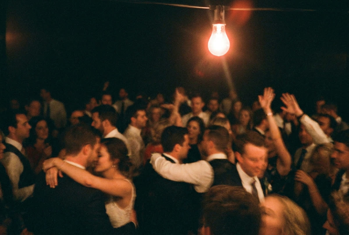 A packed dark dance floor with arms up, lit by one hanging bulb.
