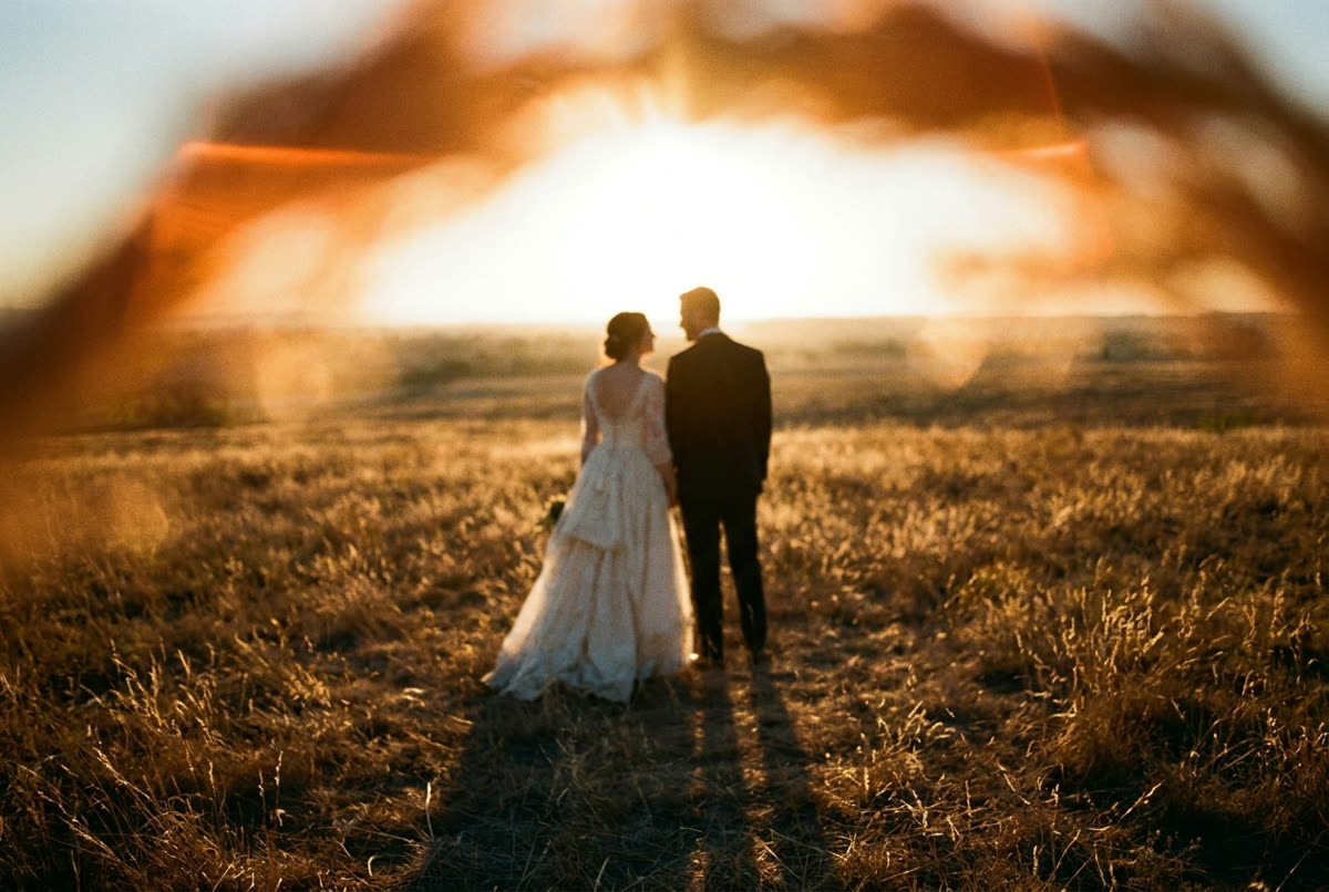 A couple in a dry paddock with the setting sun on the horizon between them.