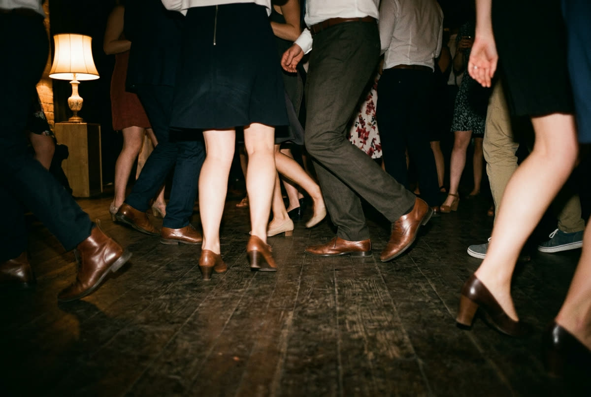 A dance floor late at night lit by one warm lamp, legs blurred with motion.