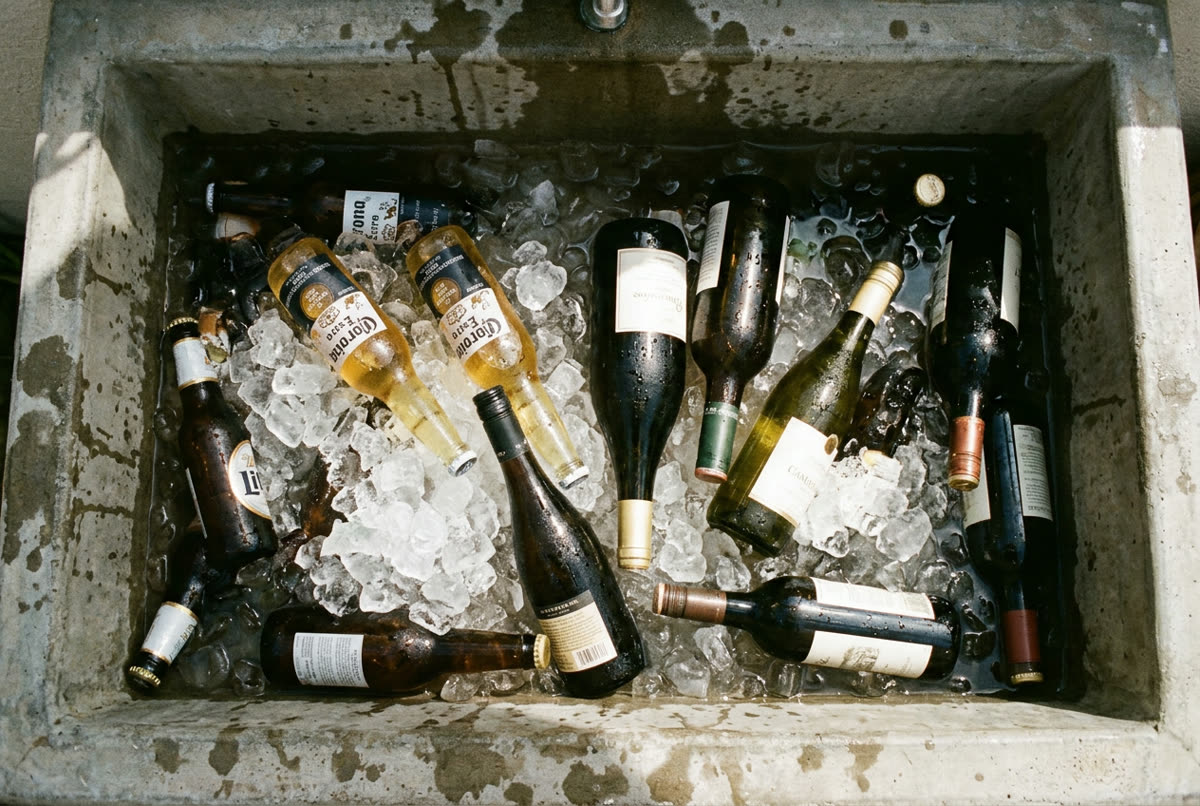 Bottles pushed into melting ice in a concrete laundry trough, hard overhead sun.