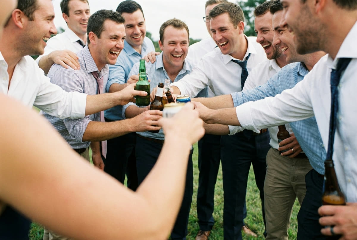 Men in untucked shirts with sleeves rolled, laughing in hard low afternoon sun.