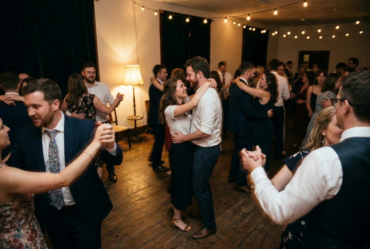 A wedding dance floor late at night lit only by string lights and one lamp, photographed from the edge of the room.
